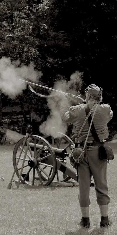 Revolutionary War Reenactment showing a soldier shooting amusket with a cannon in the background